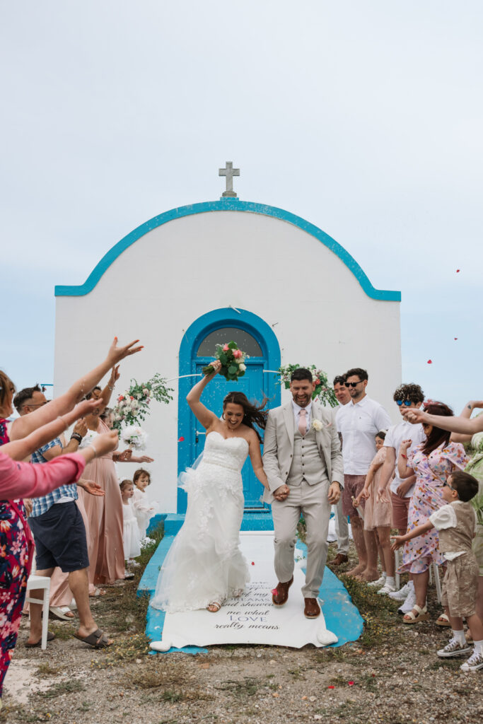 Outdoors island wedding ceremony, editorial photography, destination wedding at Agios Stephanos, Kastri island in KOS, Greece. Confetti photo with rice being thrown. Blue and white chapel.