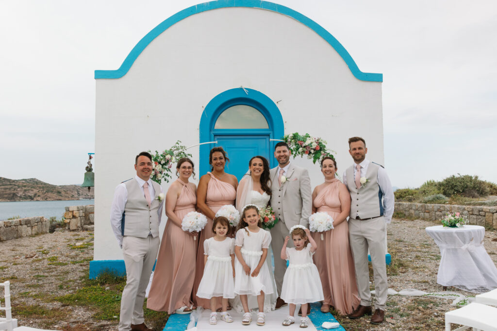 Outdoors island wedding ceremony, editorial photography, destination wedding at Agios Stephanos, Kastri island in KOS, Greece. Blue and white chapel. Bridesmaids wearing multi way pink dresses.