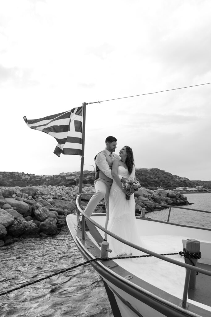 Outdoors island wedding ceremony, editorial photography, destination wedding at Agios Stephanos, Kastri island in KOS, Greece. Couple portraits on the boat that took the wedding guests from the island to the beach, with a greek flag.