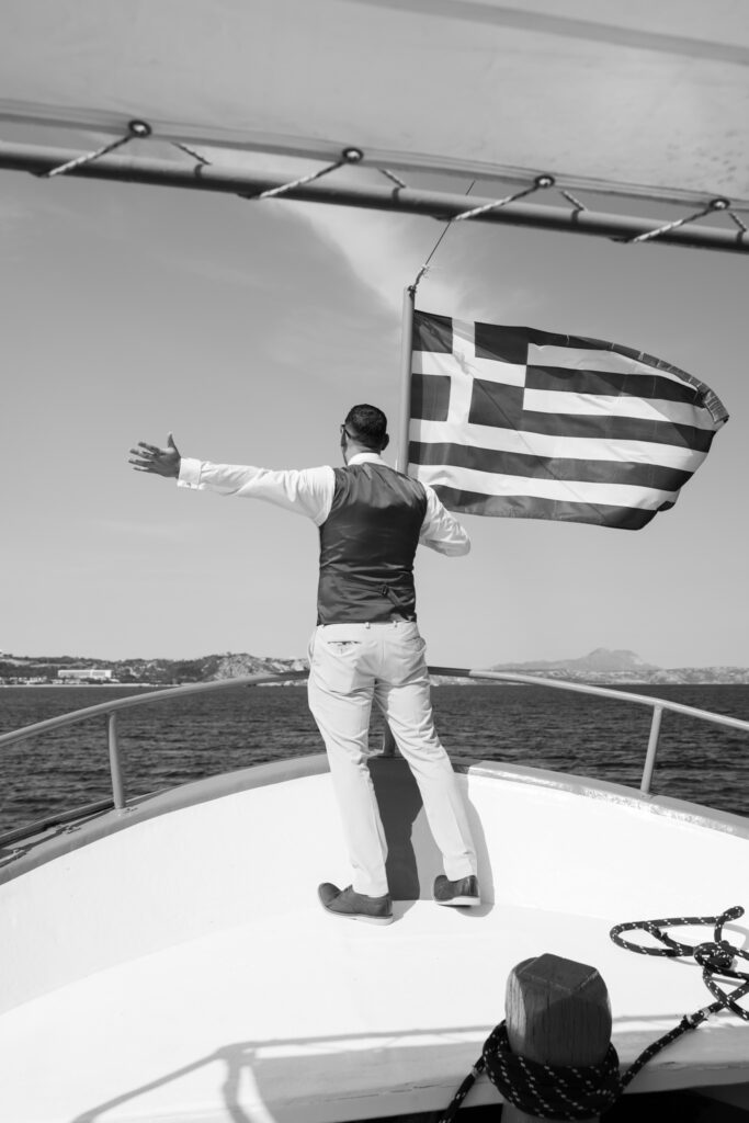 Wedding guests arriving by boat for outdoors island wedding ceremony, editorial photography, destination wedding at Agios Stephanos, Kastri island in KOS, Greece. Greek flag.