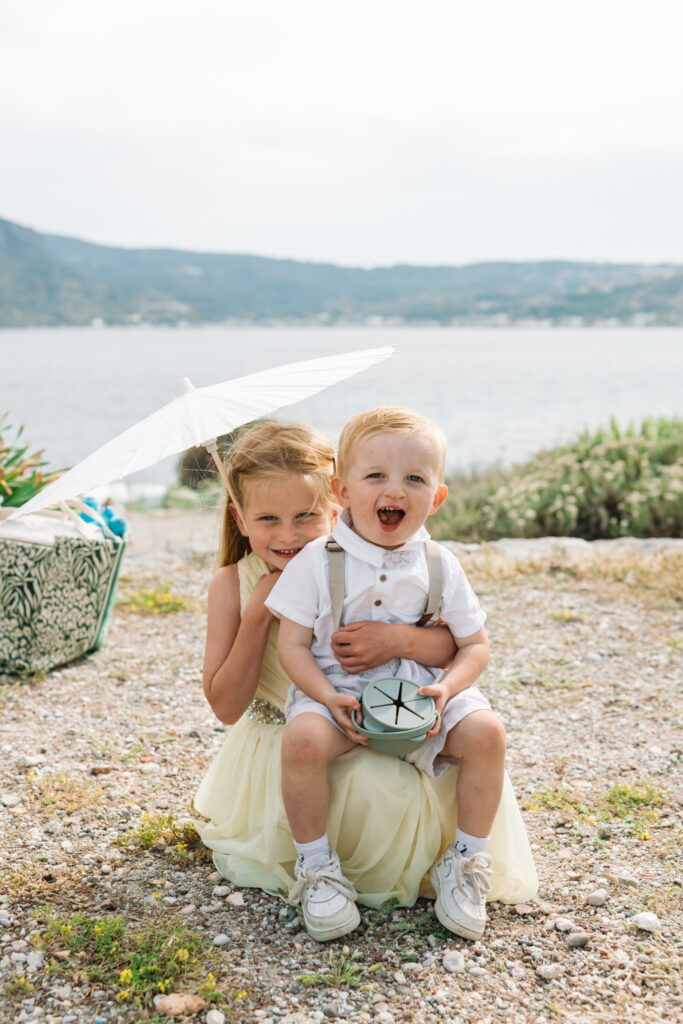 Wedding guests children with paper parasols at outdoors island wedding ceremony, editorial photography, destination wedding at Agios Stephanos, Kastri island in KOS, Greece.