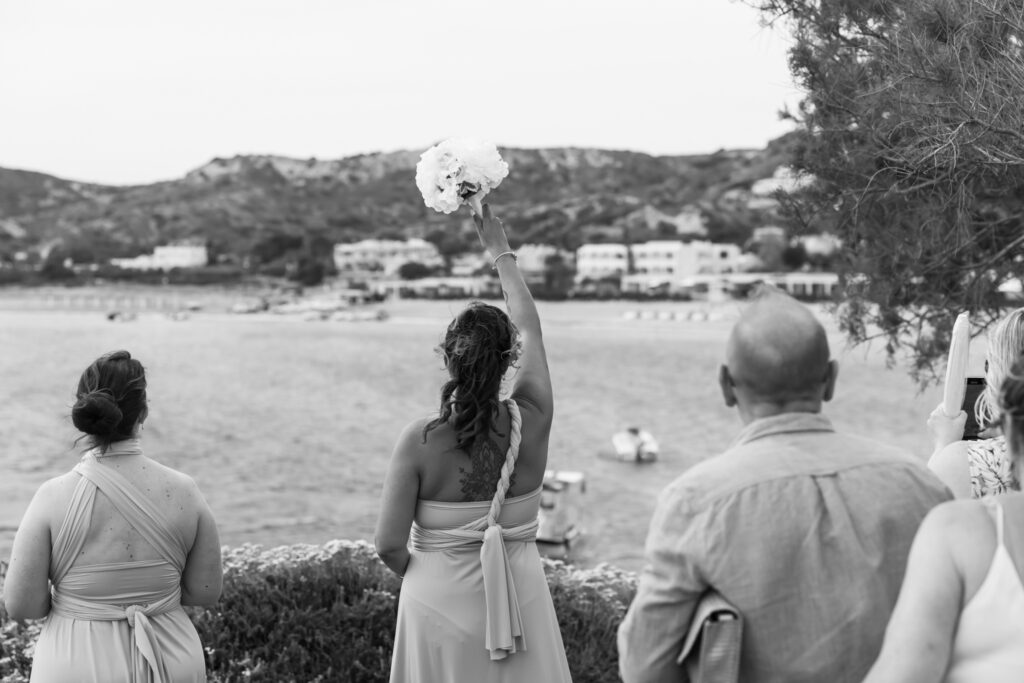 Bride arriving to the island by boat, guests waving, editorial photography, destination wedding at Agios Stephanos, Kastri island in KOS, Greece.