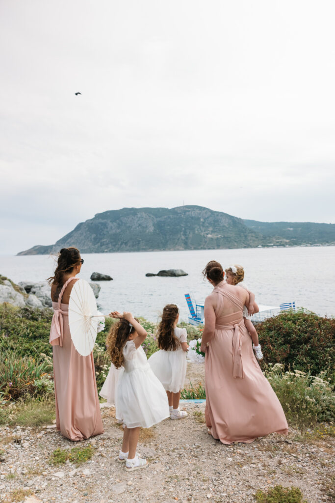 Bridesmaids and flower girls waiting for bride to arrive to the island by boat, editorial photography, destination wedding at Agios Stephanos, Kastri island in KOS, Greece. Bridesmaid wearing pink dress.