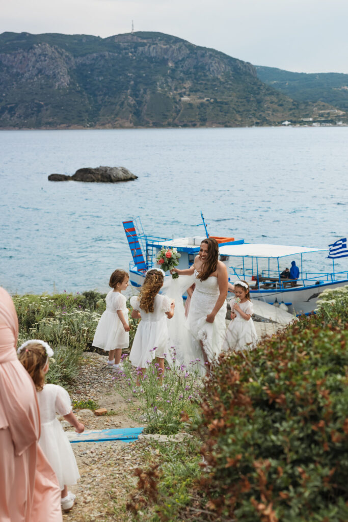 Bridesmaids and flower girls waiting for bride to arrive to the island by boat, editorial photography, destination wedding at Agios Stephanos, Kastri island in KOS, Greece. Bridesmaid wearing pink dress.