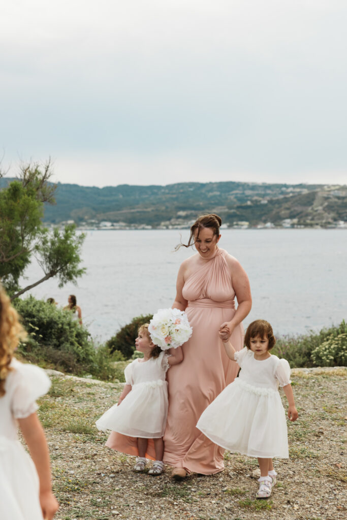 Bridesmaids walking down the aisle with her bridesmaid, editorial photography, destination wedding at Agios Stephanos, Kastri island in KOS, Greece. Bridesmaid wearing pink dress.