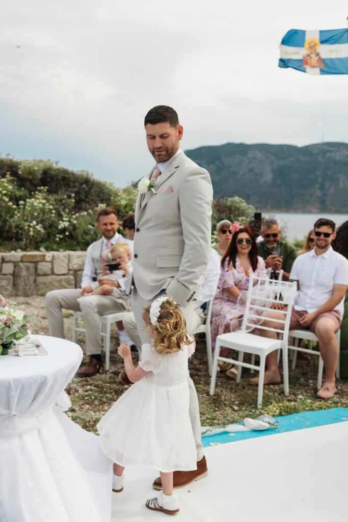 Groom waiting at the alter for his bride, editorial photography, destination wedding at Agios Stephanos, Kastri island in KOS, Greece. Groom wearing light beige suit and baby pink tie.