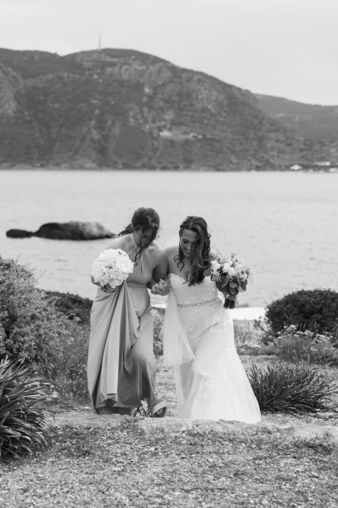 Bride walking down the aisle with her bridesmaid, black and white editorial photography, destination wedding at Agios Stephanos, Kastri island in KOS, Greece