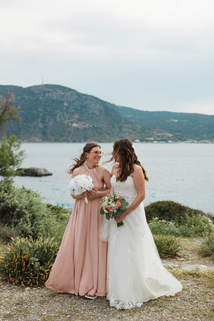 Bride walking down the aisle with her bridesmaid, editorial photography, destination wedding at Agios Stephanos, Kastri island in KOS, Greece. Bridesmaid wearing pink dress.