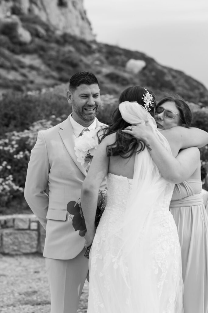 Groom waiting at the alter for his bride, black and white editorial photography, destination wedding at Agios Stephanos, Kastri island in KOS, Greece. Groom wearing light beige suit and baby pink tie.