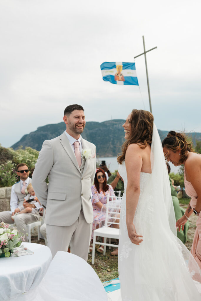 Groom waiting at the alter for his bride, editorial photography, destination wedding at Agios Stephanos, Kastri island in KOS, Greece. Groom wearing light beige suit and baby pink tie.