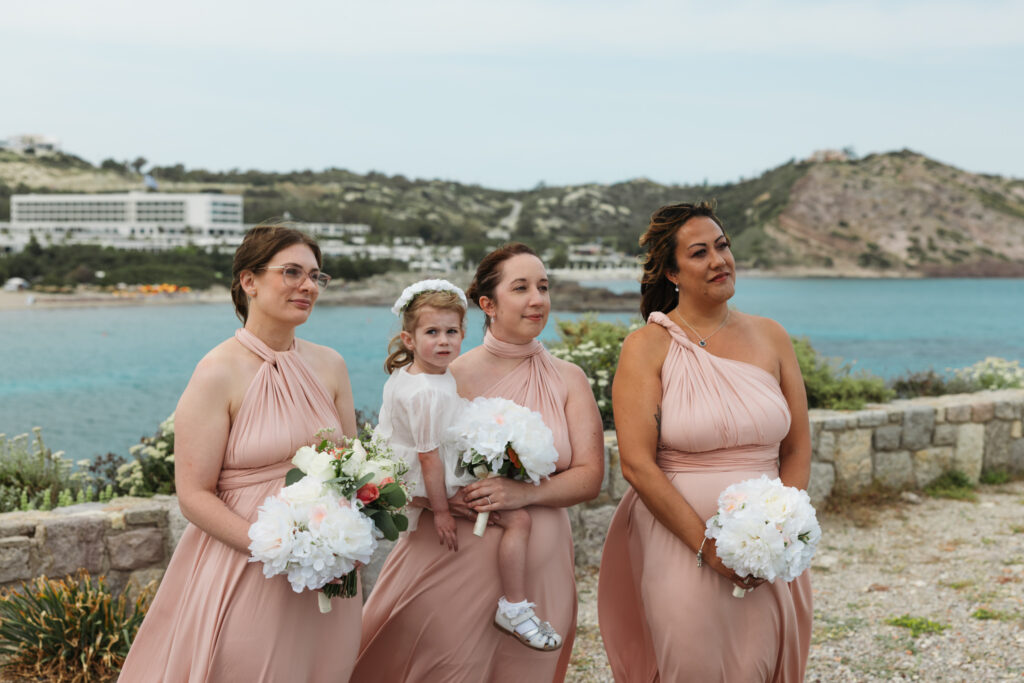Outdoors island wedding ceremony, editorial photography, destination wedding at Agios Stephanos, Kastri island in KOS, Greece. Bridesmaids wearing multi way pink dresses.