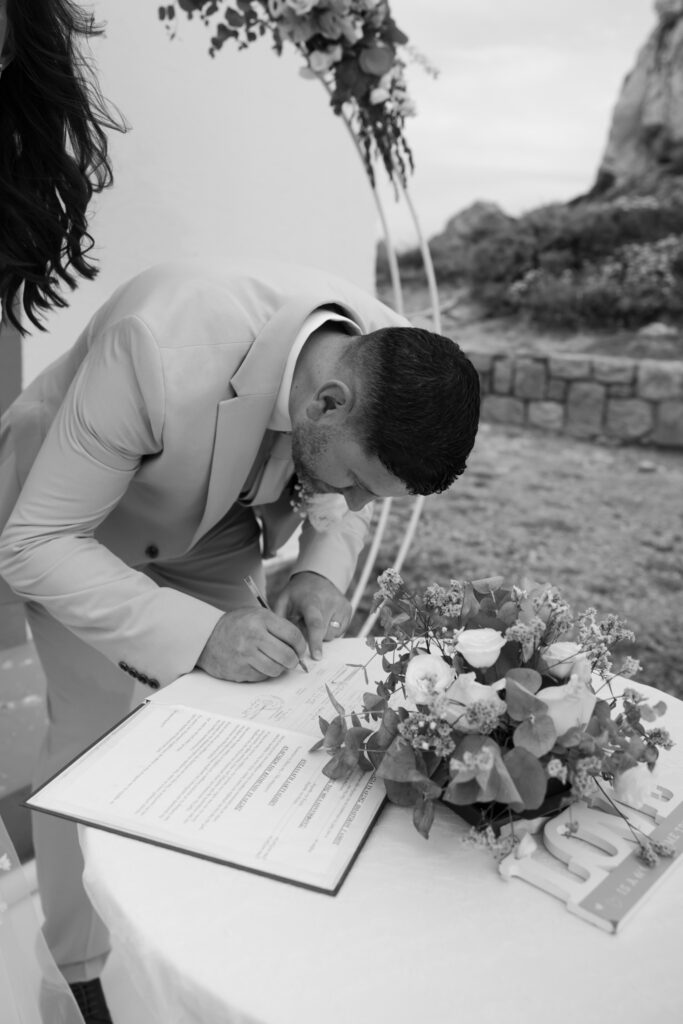 Outdoors island wedding ceremony, editorial photography, destination wedding at Agios Stephanos, Kastri island in KOS, Greece. Groom signing papers.