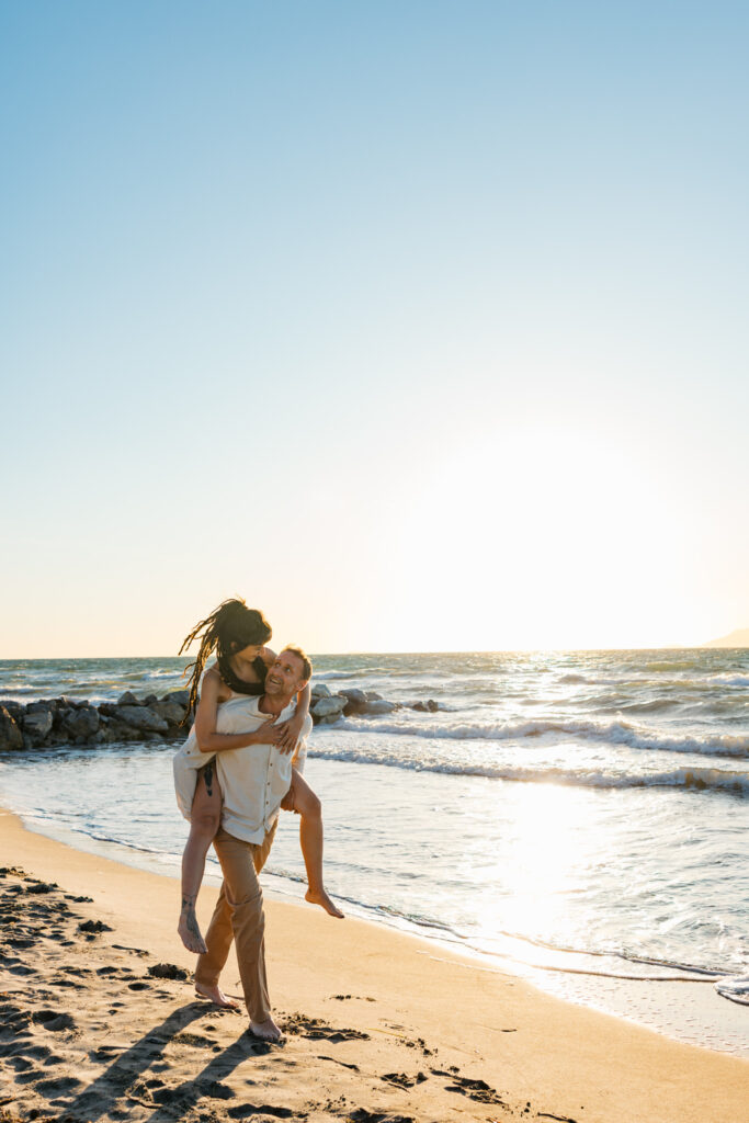 Romantic storytelling portrait of Greek and Italian couple walking barefoot on Kos beach at golden hour — destination wedding photographer Greece. Editorial photography, engagement beach sunset session.