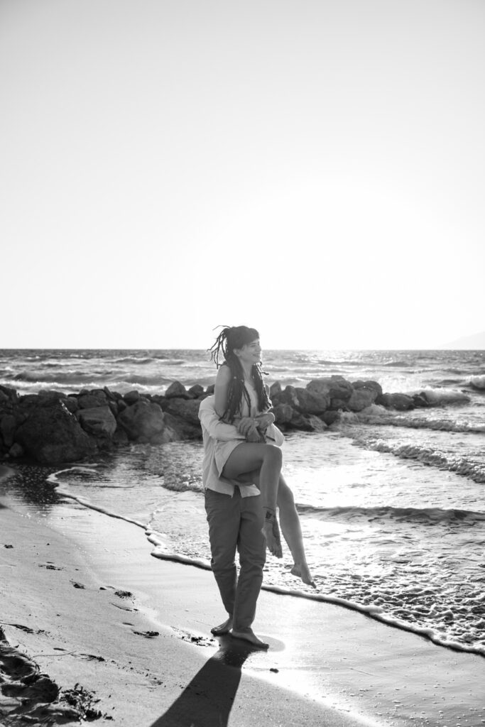 Romantic storytelling portrait of Greek and Italian couple walking barefoot on Kos beach at golden hour — destination wedding photographer Greece. Editorial photography, engagement beach sunset session.