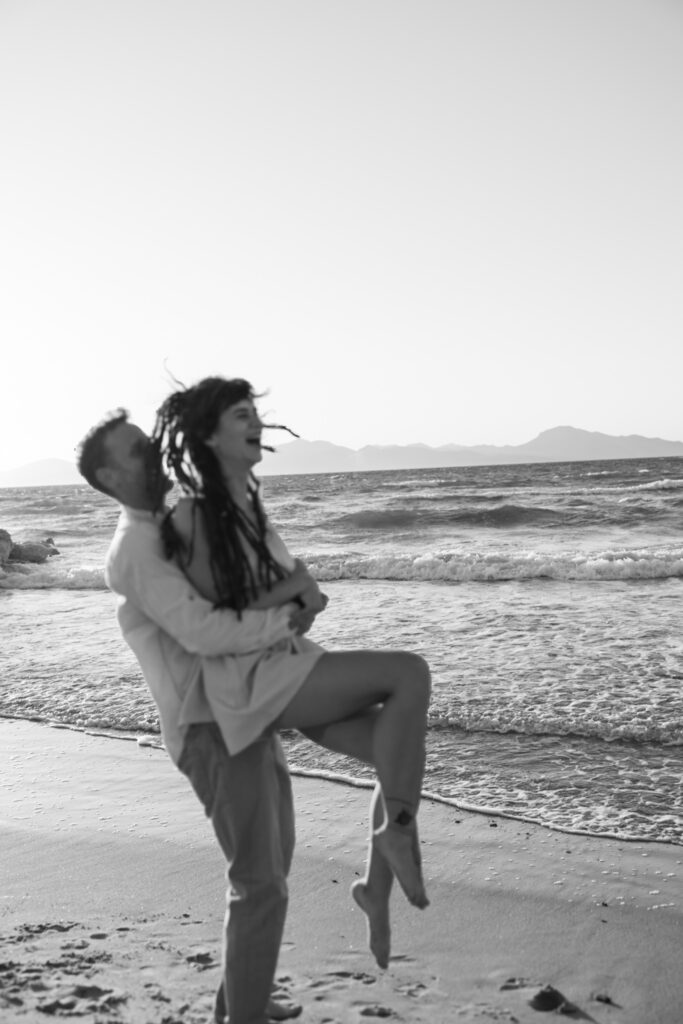 Romantic storytelling portrait of Greek and Italian couple walking barefoot on Kos beach at golden hour — destination wedding photographer Greece. Editorial photography, engagement beach sunset session.