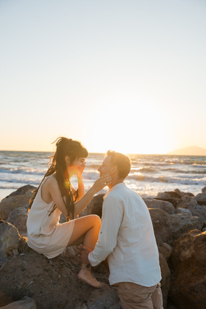 Romantic storytelling portrait of Greek and Italian couple walking barefoot on Kos beach at golden hour — destination wedding photographer Greece. Editorial photography, engagement beach sunset session.