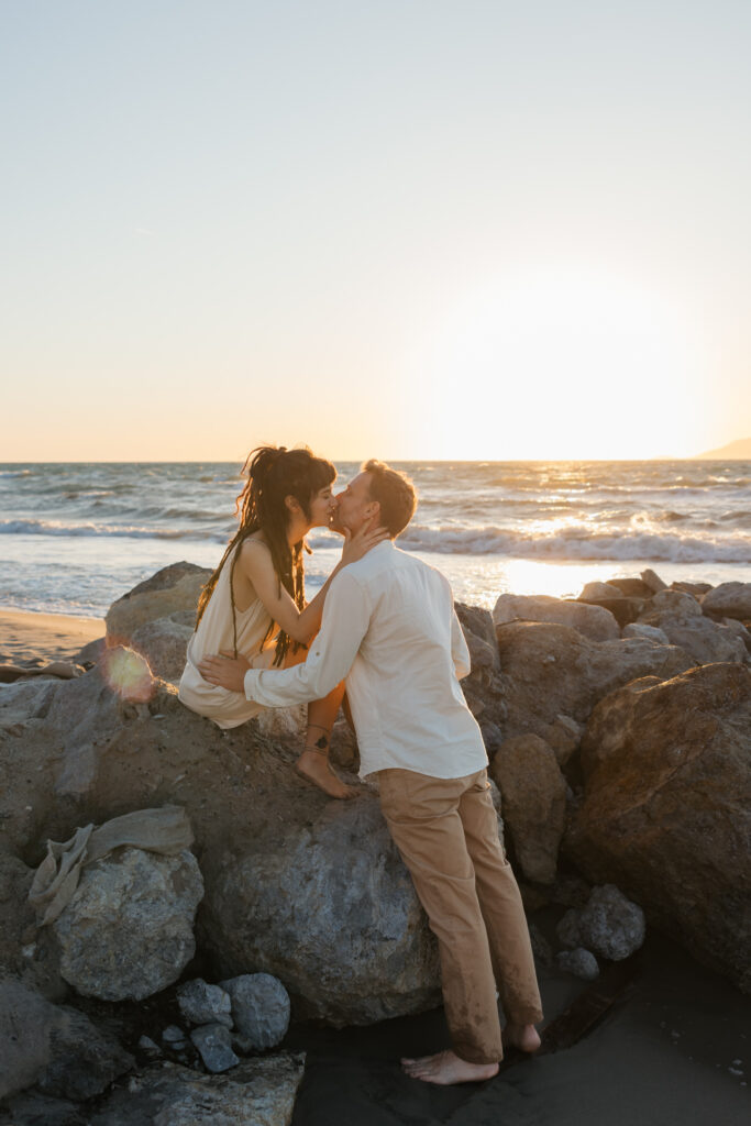 Romantic storytelling portrait of Greek and Italian couple walking barefoot on Kos beach at golden hour — destination wedding photographer Greece. Editorial photography, engagement beach sunset session.