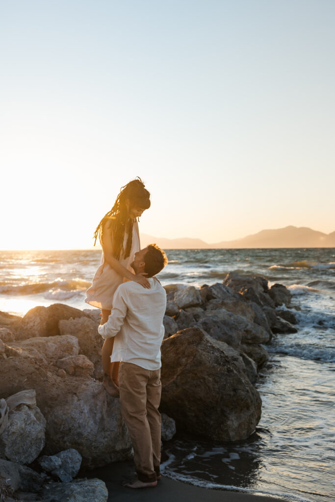 Romantic storytelling portrait of Greek and Italian couple walking barefoot on Kos beach at golden hour — destination wedding photographer Greece. Editorial photography, engagement beach sunset session.