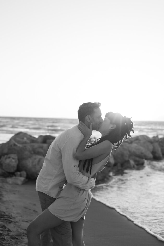 Romantic storytelling portrait of Greek and Italian couple walking barefoot on Kos beach at golden hour — destination wedding photographer Greece. Editorial photography, engagement beach sunset session.