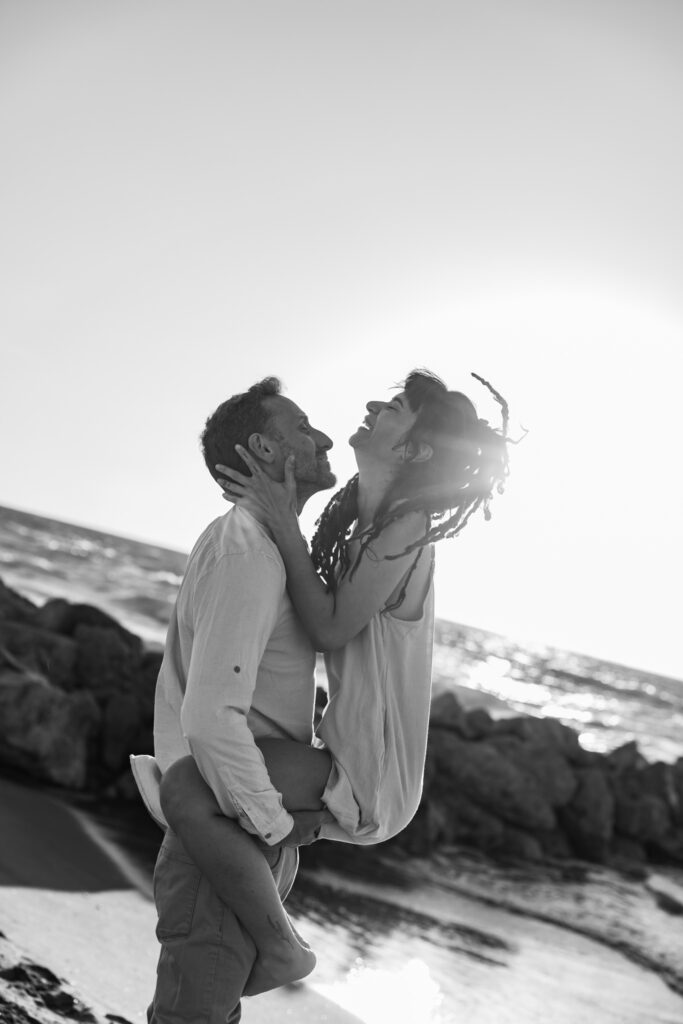 Romantic storytelling portrait of Greek and Italian couple walking barefoot on Kos beach at golden hour — destination wedding photographer Greece. Editorial photography, engagement beach sunset session.
