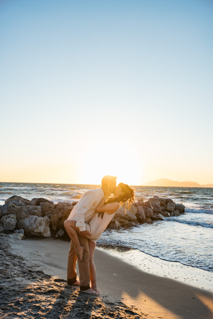 Romantic storytelling portrait of Greek and Italian couple walking barefoot on Kos beach at golden hour — destination wedding photographer Greece. Editorial photography, engagement beach sunset session.