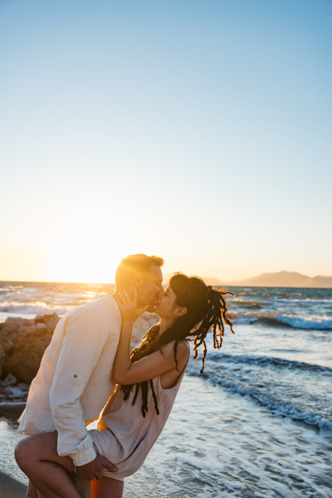Romantic storytelling portrait of Greek and Italian couple walking barefoot on Kos beach at golden hour — destination wedding photographer Greece. Editorial photography, engagement beach sunset session.