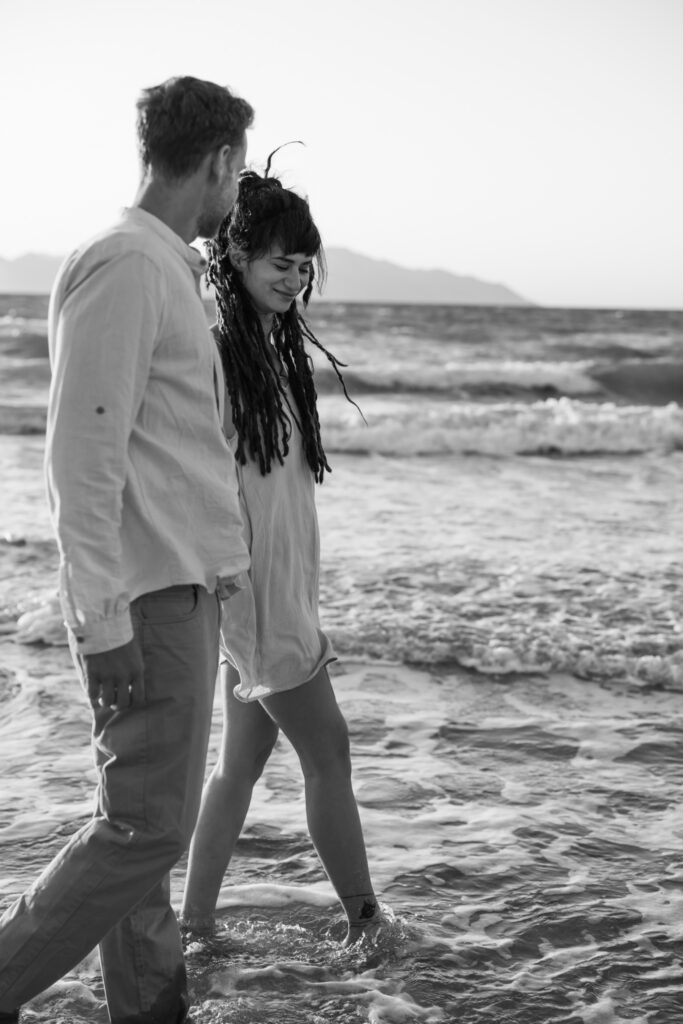 Romantic storytelling portrait of Greek and Italian couple walking barefoot on Kos beach at golden hour — destination wedding photographer Greece. Editorial photography, engagement beach sunset session.