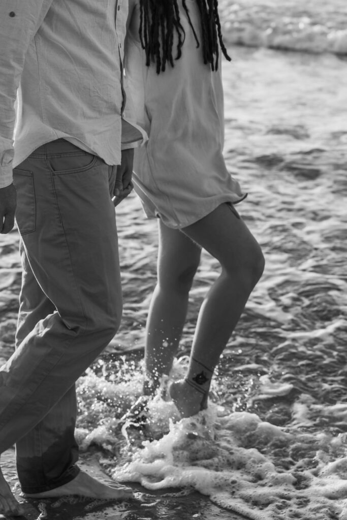 Romantic storytelling portrait of Greek and Italian couple walking barefoot on Kos beach at golden hour — destination wedding photographer Greece. Editorial photography, engagement beach sunset session.