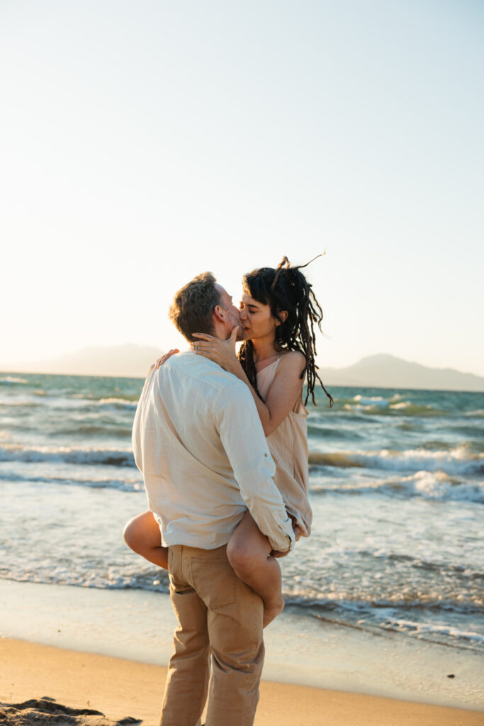 Romantic storytelling portrait of Greek and Italian couple walking barefoot on Kos beach at golden hour — destination wedding photographer Greece. Editorial photography, engagement beach sunset session.