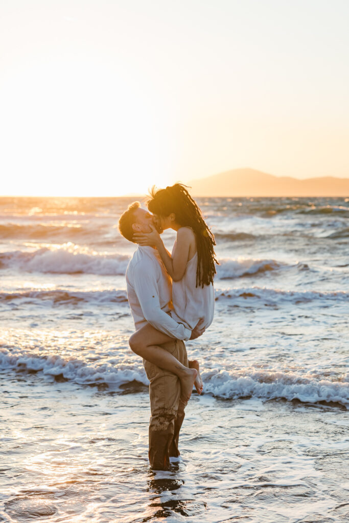 Romantic storytelling portrait of Greek and Italian couple walking barefoot on Kos beach at golden hour — destination wedding photographer Greece. Editorial photography, engagement beach sunset session.