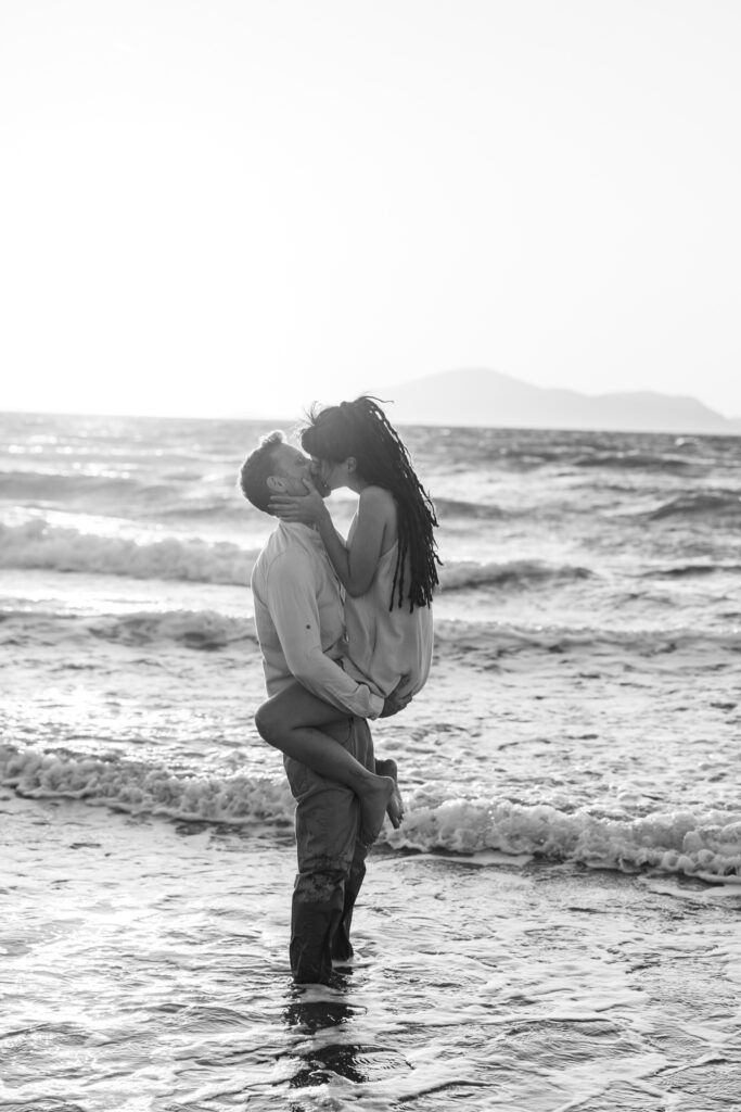 Romantic storytelling portrait of Greek and Italian couple walking barefoot on Kos beach at golden hour — destination wedding photographer Greece. Editorial photography, engagement beach sunset session.