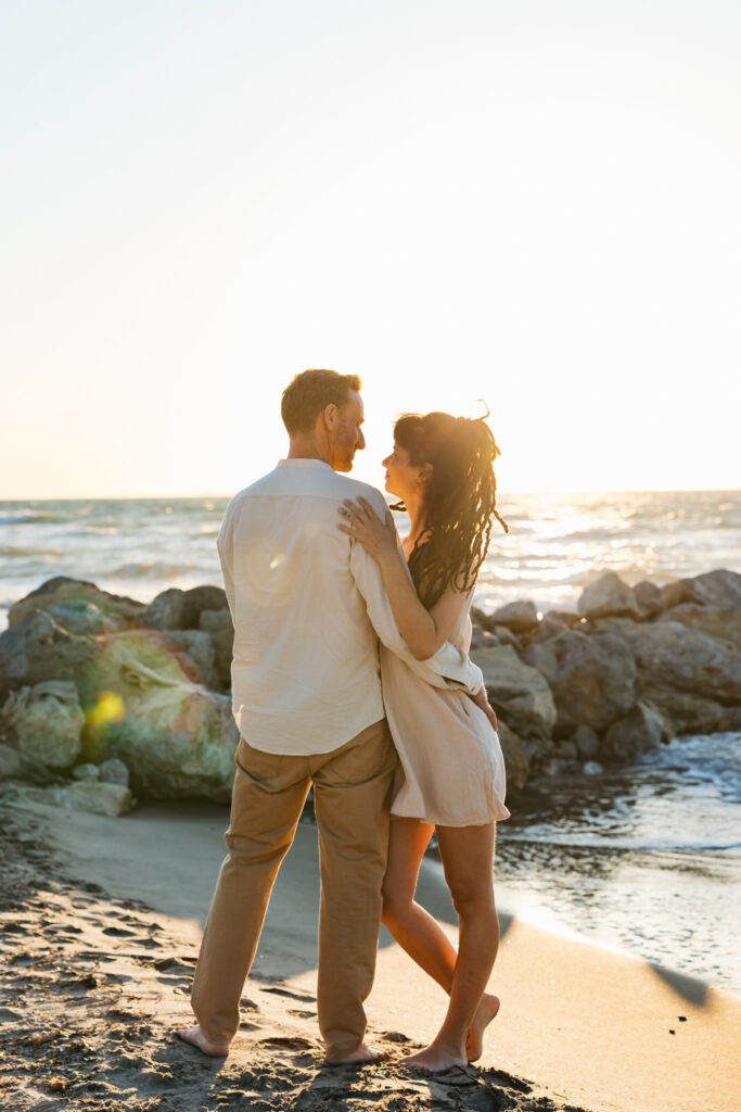 Romantic storytelling portrait of Greek and Italian couple walking barefoot on Kos beach at golden hour — destination wedding photographer Greece. Editorial photography, engagement beach sunset session.